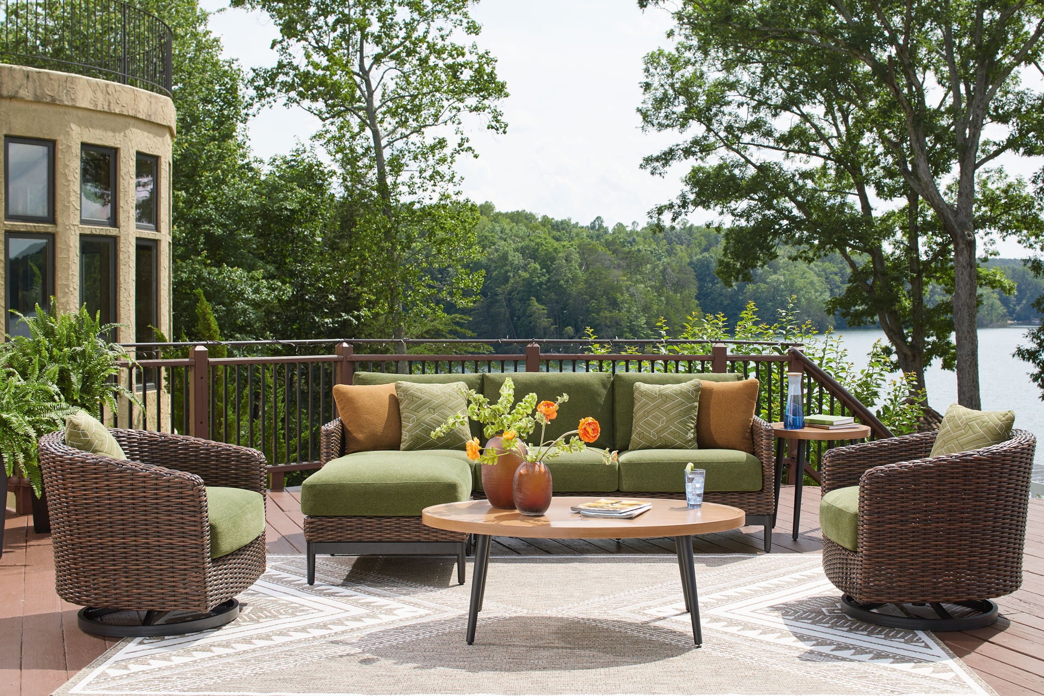 Wicker lounge set with green sofa cushions, armchairs, and round coffee table with vases