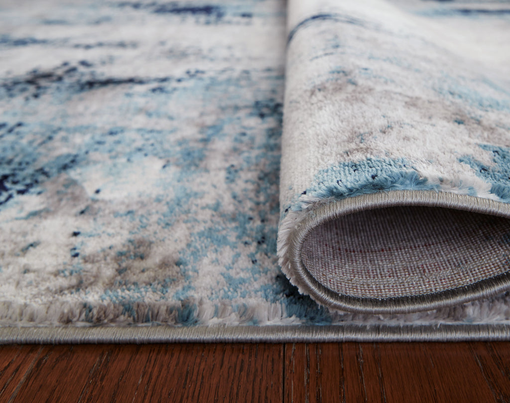 Rolled corner of blue and gray abstract rug with stitched border