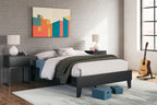Dark platform bed with white pillows and folded bedding on mattress