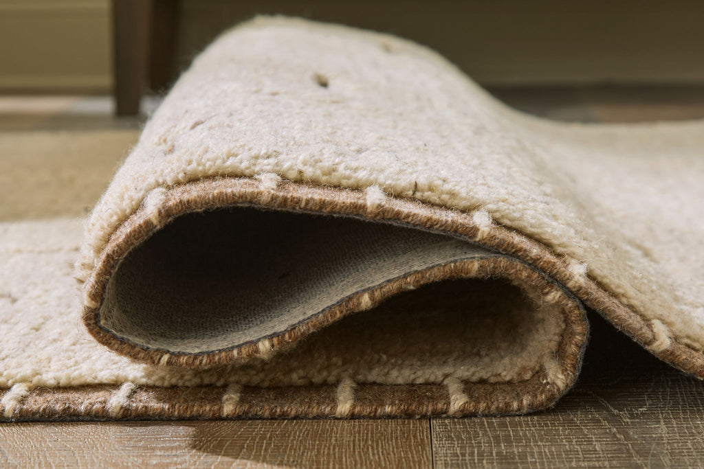 Beige rug edge with short pile and visible underside binding