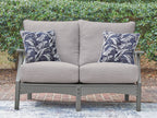 Gray loveseat with two blue palm-pattern throw pillows and padded seat cushions