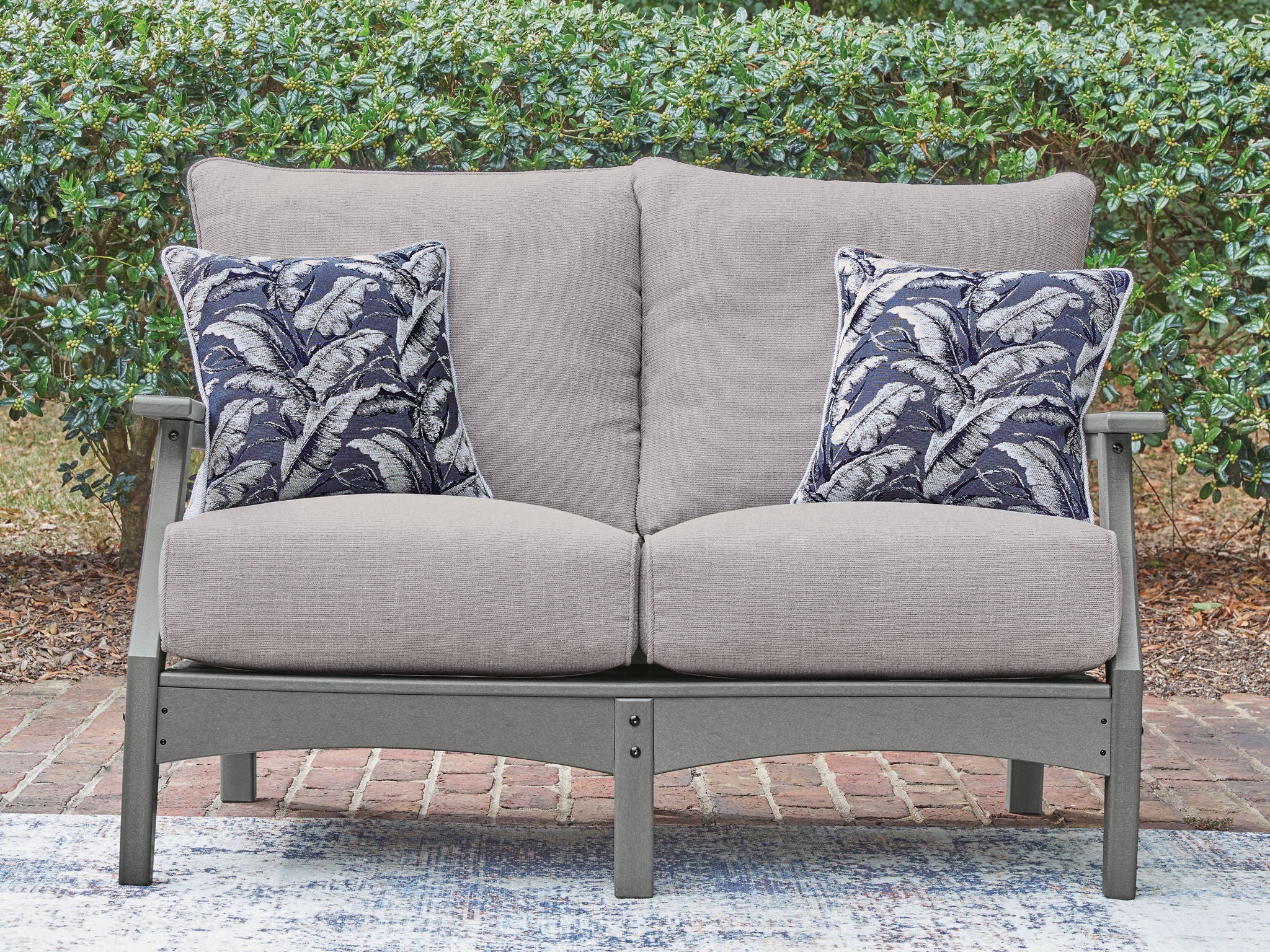 Gray loveseat with two blue palm-pattern throw pillows and padded seat cushions