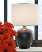 Ceramic table lamp with black speckled base and white drum shade near orange flowers