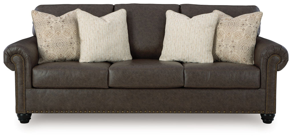 Dark brown sofa with four beige patterned pillows, rolled arms, and studded base