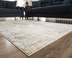 Cream abstract area rug with blue-gray distressed pattern placed between dark sofas.