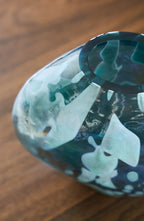 Blue glass vase close-up, curved shoulder and glossy abstract paint-like pattern