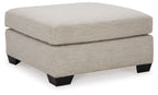 Oversized ottoman with light beige fabric, thick cushioned top and squared black legs.