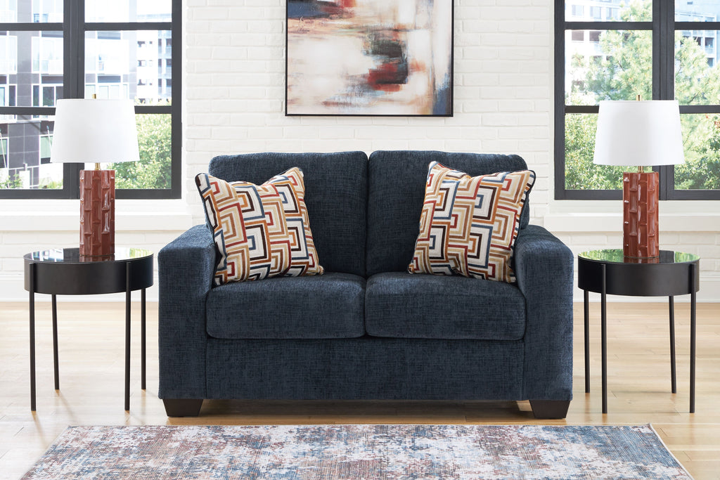 Dark navy loveseat with two patterned throw pillows and wide, cushioned arms.