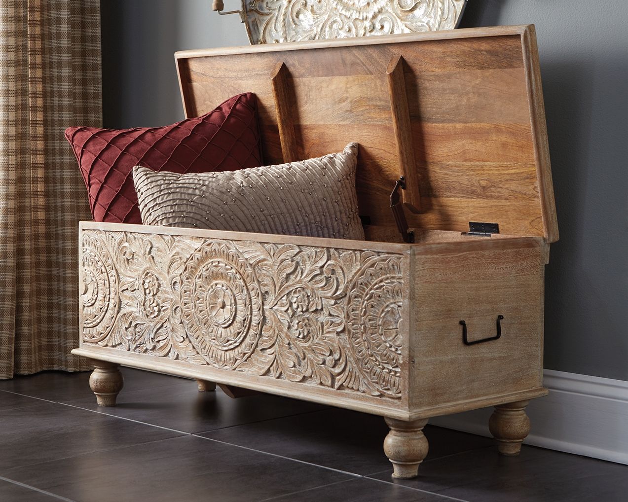 Open beige storage bench with carved front, lift-up lid, and cushioned contents