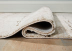 Beige rug edge with rolled finish and visible underside, low pile.