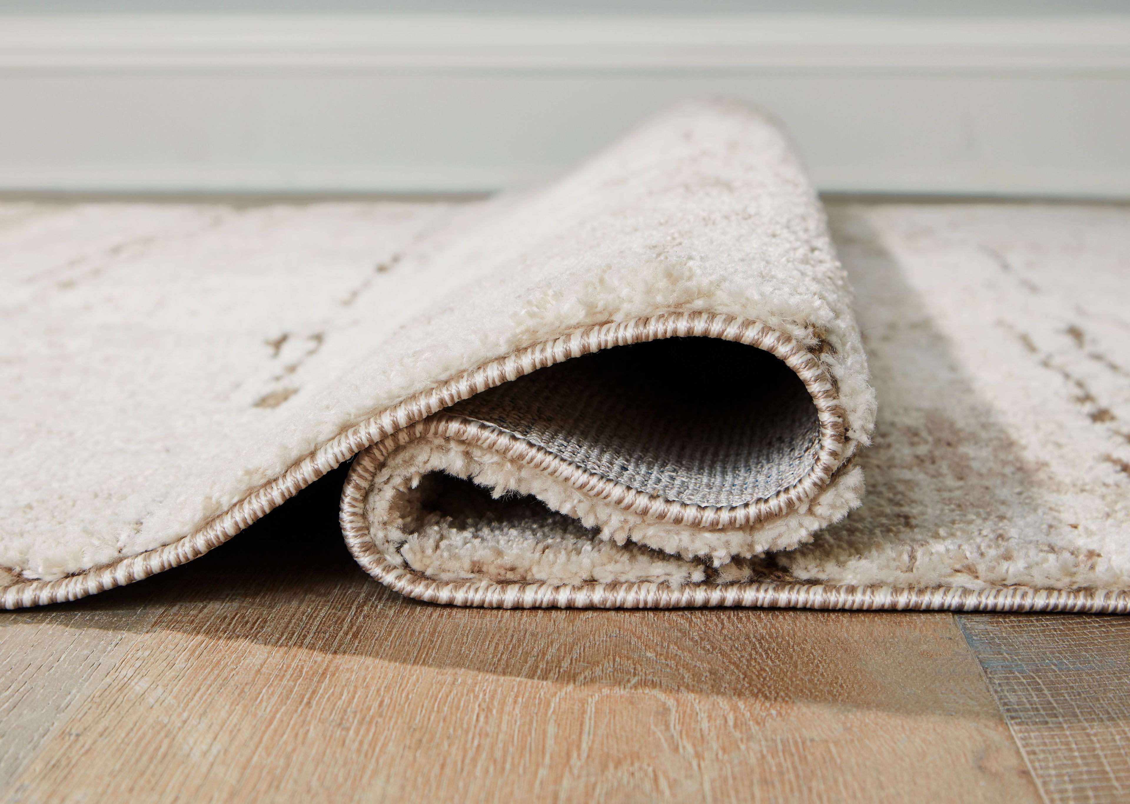Beige rug edge with rolled finish and visible underside, low pile.