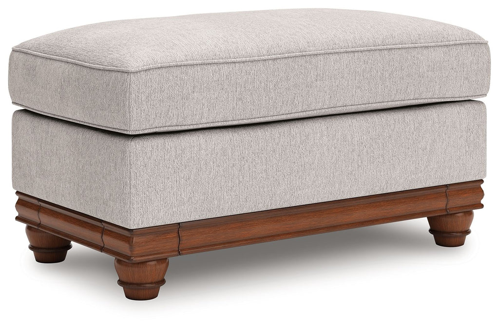 Sandstone upholstered ottoman with padded seat, wood base, and turned legs