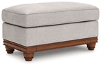 Sandstone upholstered ottoman with padded seat, wood base, and turned legs