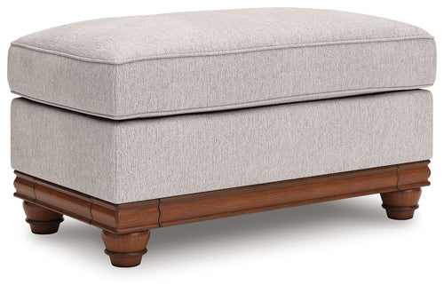Sandstone upholstered ottoman with padded seat, wood base, and turned legs