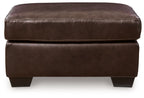 Dark brown upholstered ottoman with cushioned top, visible double-stitching, block legs