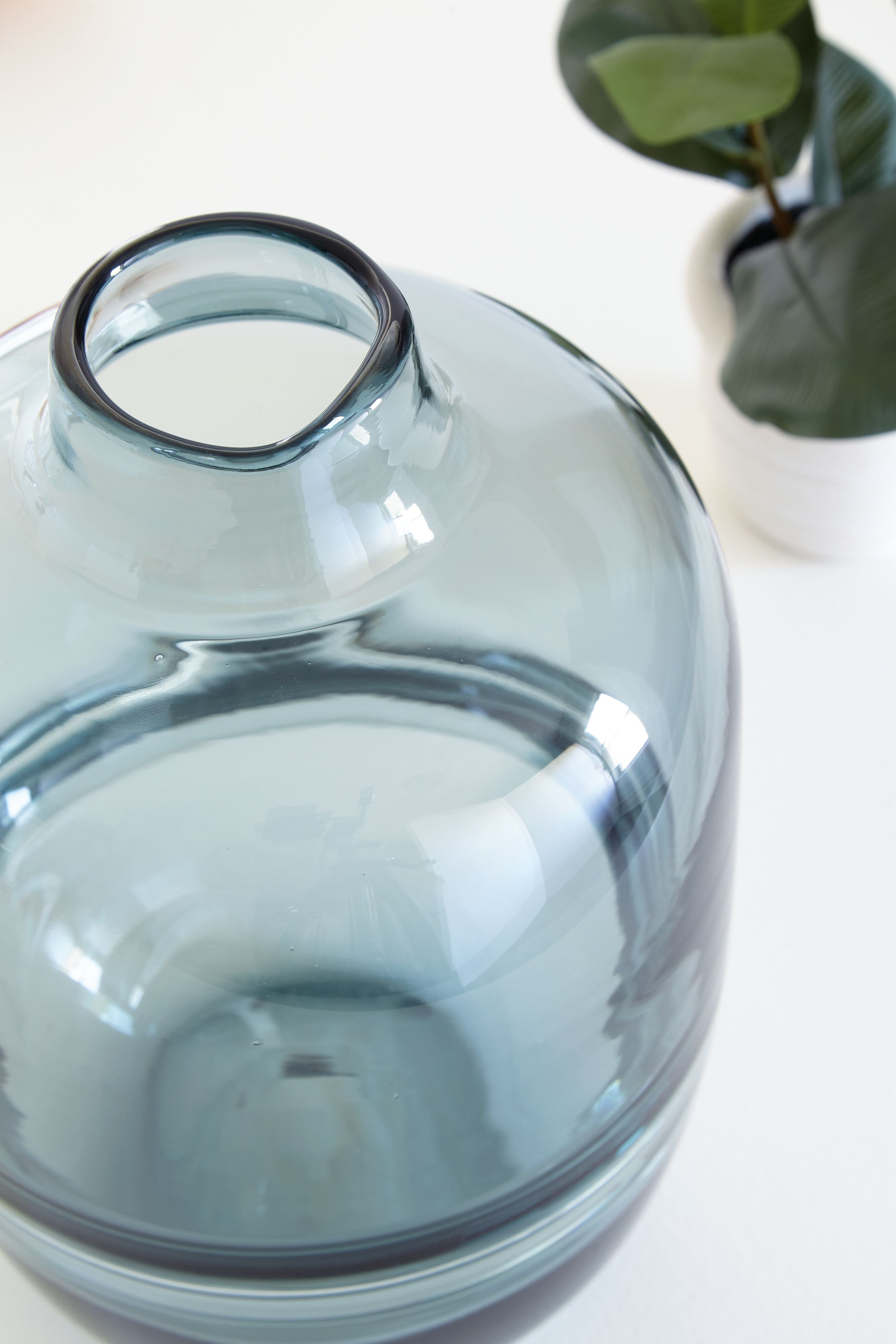 Teal glass vase close-up from side, rounded shoulder and flared mouth.
