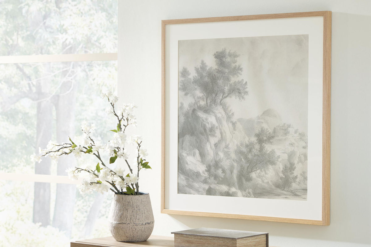 Framed gray landscape wall art on display with vase of white flowers