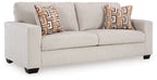 Light beige upholstered sofa with two patterned geometric throw pillows.