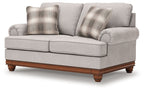 Upholstered loveseat in light sand fabric with plaid throw pillows and rolled arms