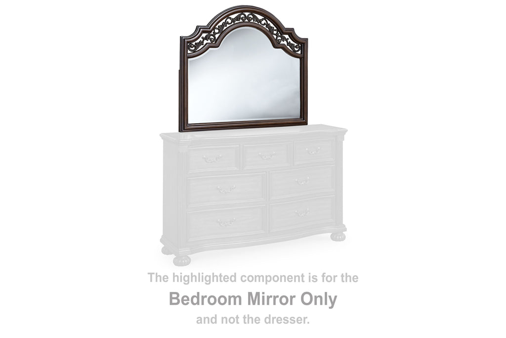 Arched brown bedroom mirror on white dresser with ornate carved frame