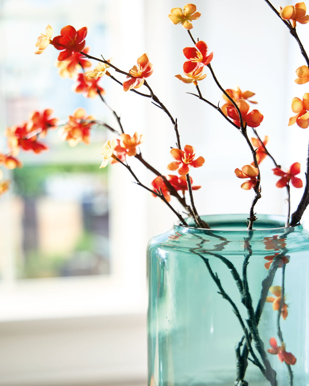 Teal glass vase with orange and yellow blossoms on dark stems
