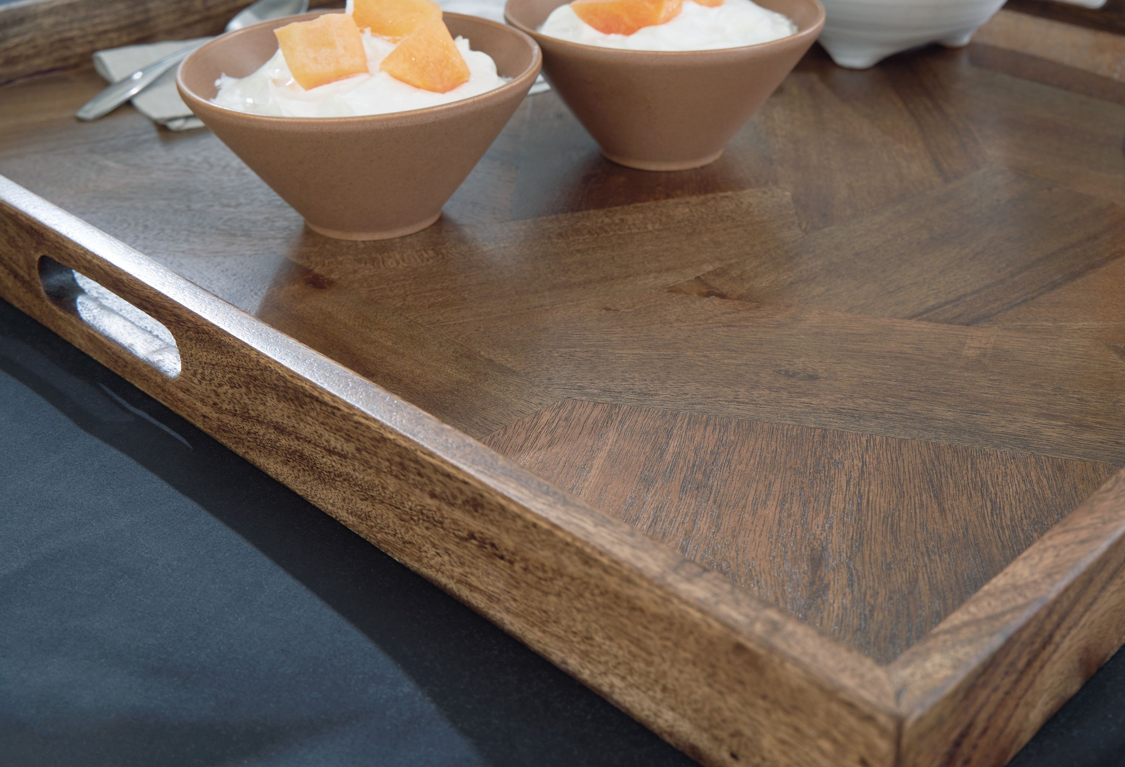 Brown wooden tray with side cutout handle, egg cups and mugs on top.