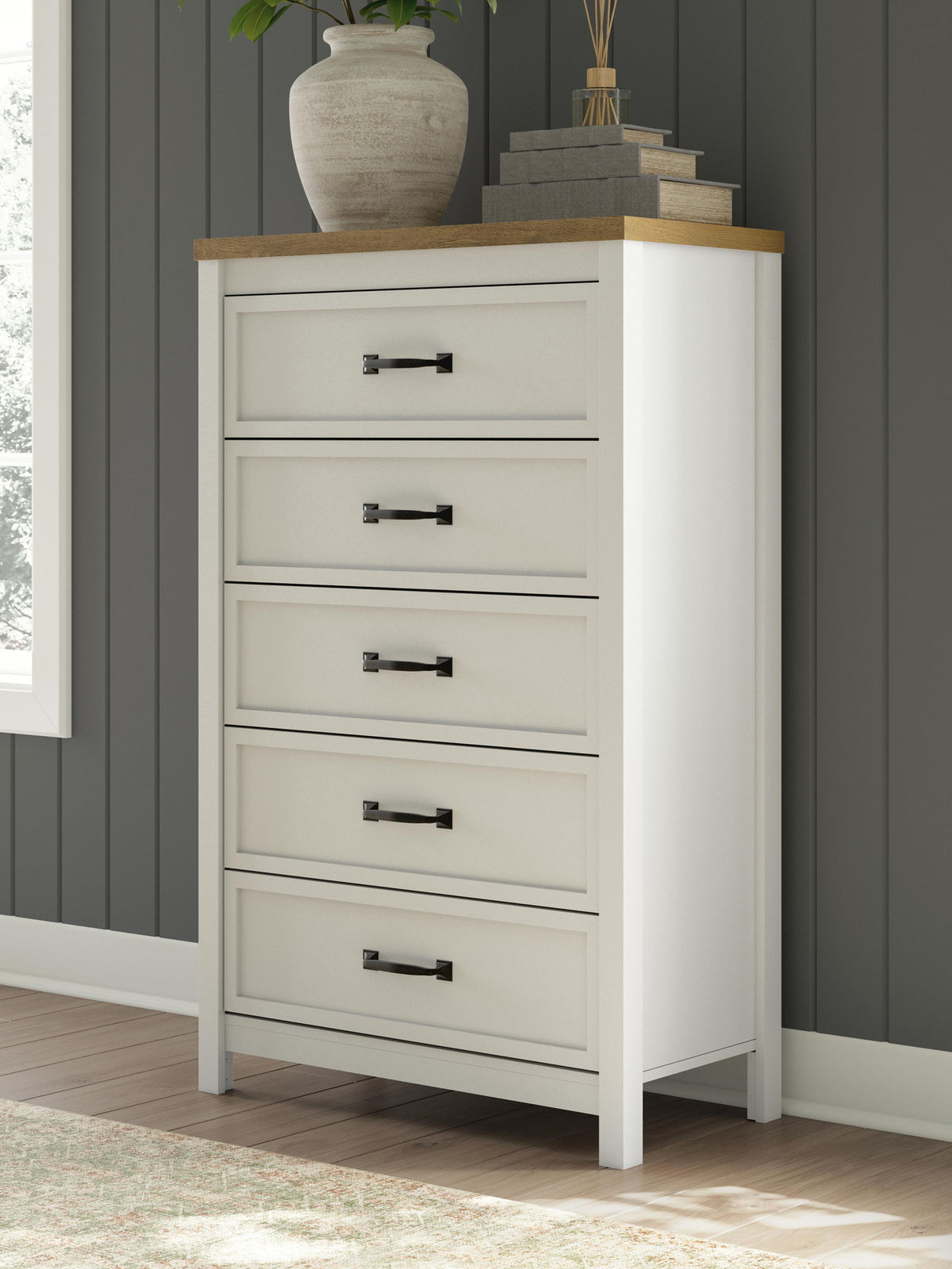 White five-drawer chest with brown top and black bar pulls, styled with decor