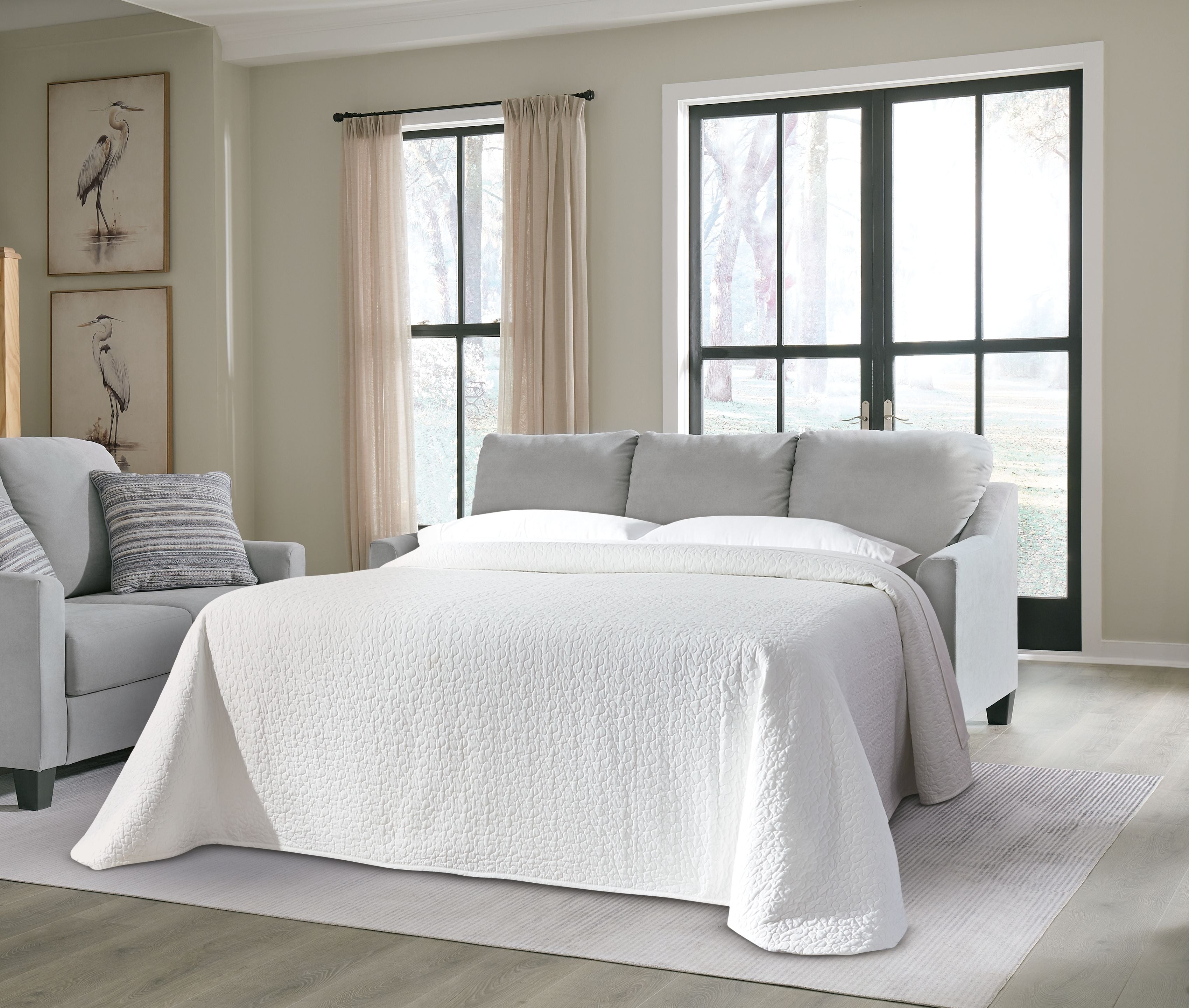 Gray queen sofa sleeper styled as a bed with white quilt, pillows, and striped shams