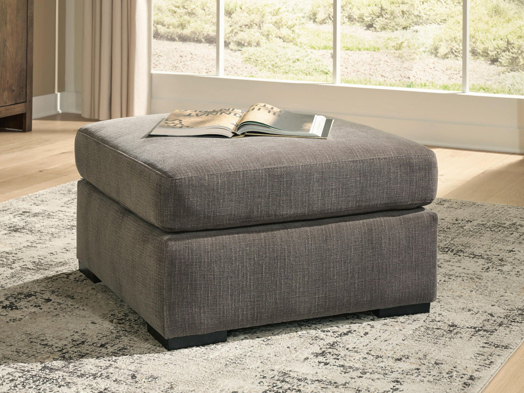 Gray upholstered accent ottoman with square silhouette, cushioned top, and block legs