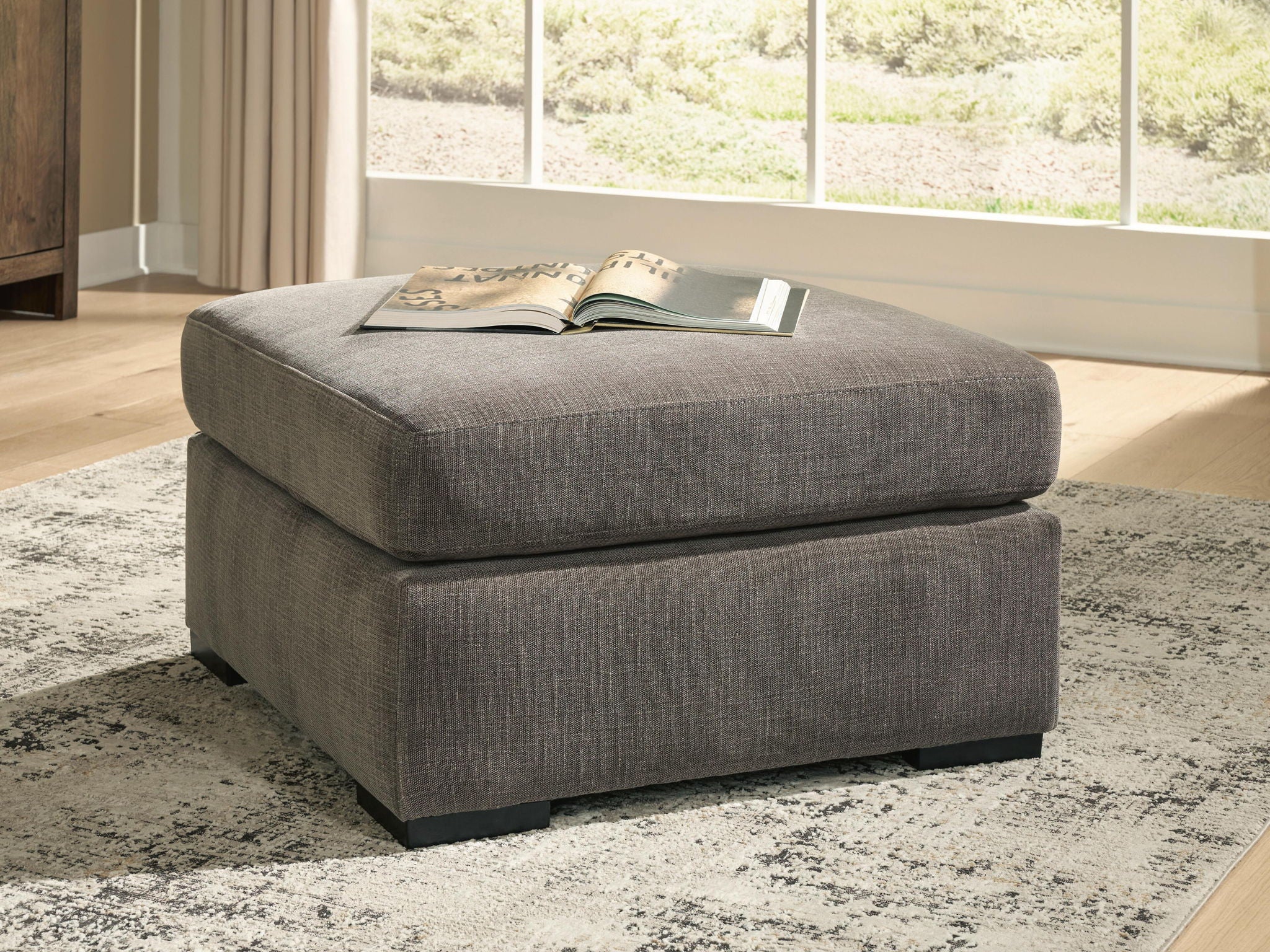 Gray upholstered accent ottoman with square silhouette, cushioned top, and block legs