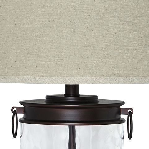 Bronze-finish hardware on clear glass table lamp with beige drum shade