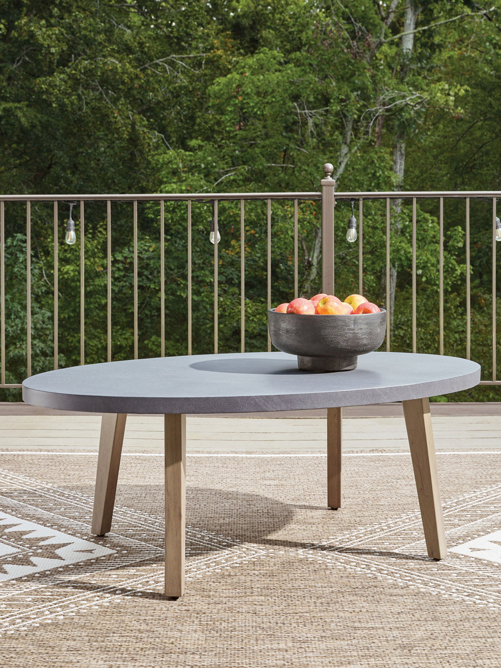 Outdoor oval gray cocktail table with tapered wood legs and fruit bowl