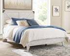 Panel bed with whitewashed wood frame and paneled headboard, white bedding with blue covers