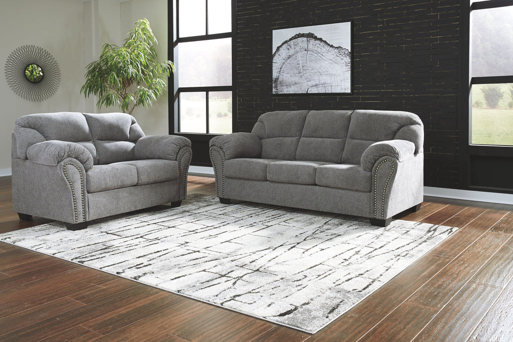 Dark gray sofa and loveseat set with tufted backs, rolled arms, and studded trim