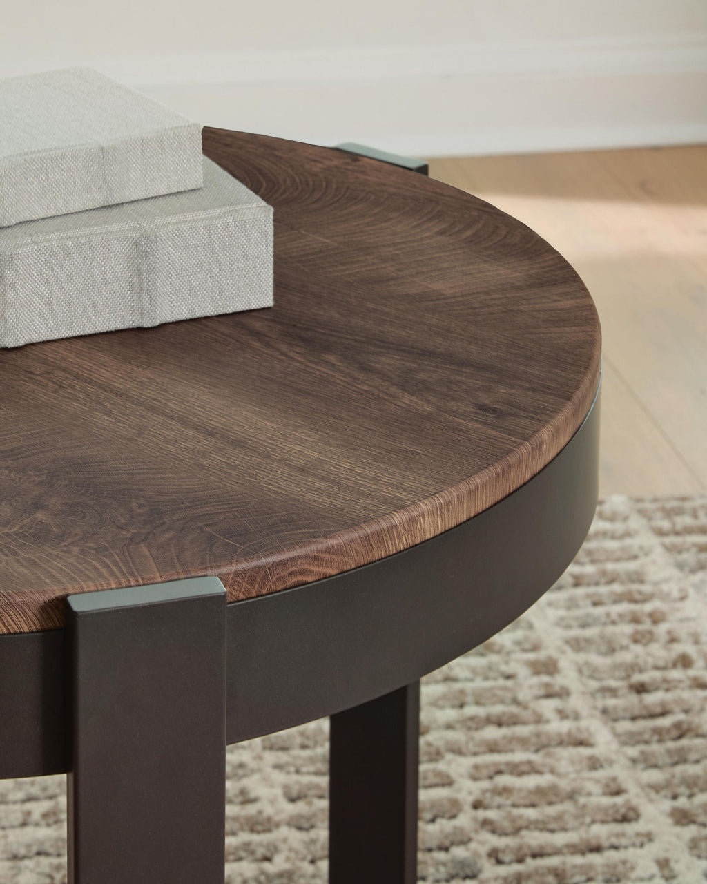 Round table top with brown wood grain and dark curved base, close-up