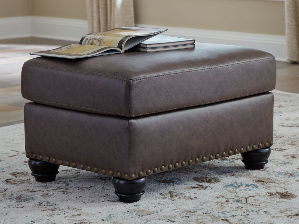 Dark brown ottoman with nailhead trim on sides and turned wood legs