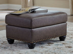 Dark brown ottoman with nailhead trim on sides and turned wood legs
