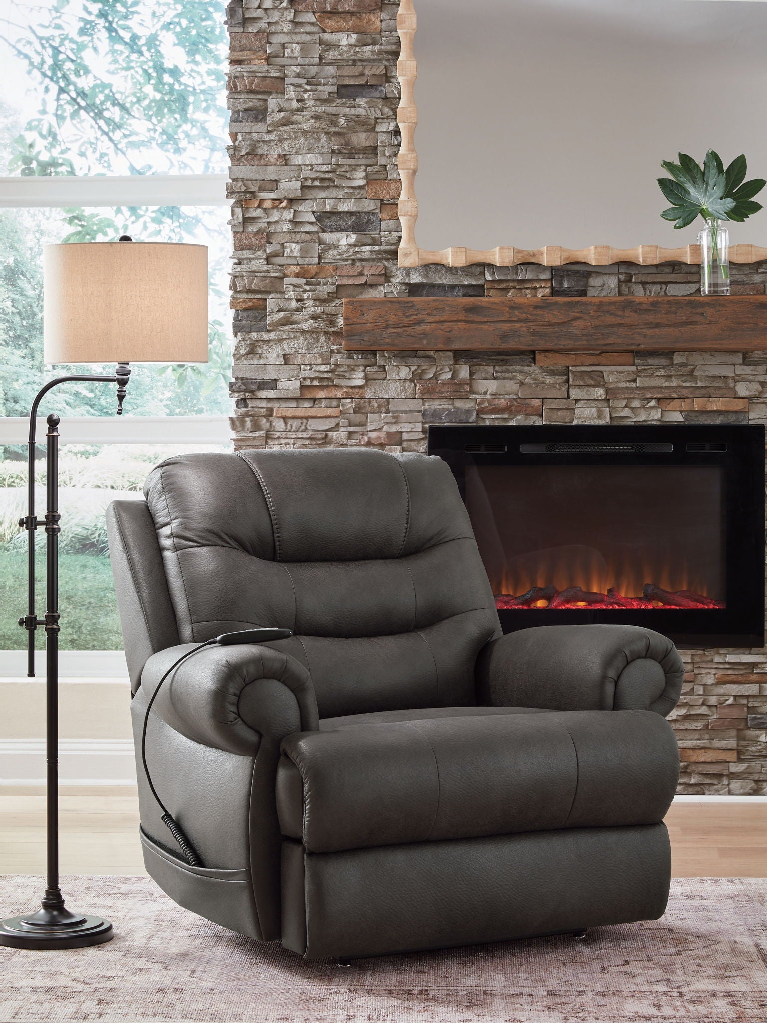 Dark gray leather-look power lift recliner beside fireplace with padded head and arms