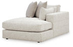 Corner chaise ottoman with light beige upholstery and stacked back pillows, rounded end
