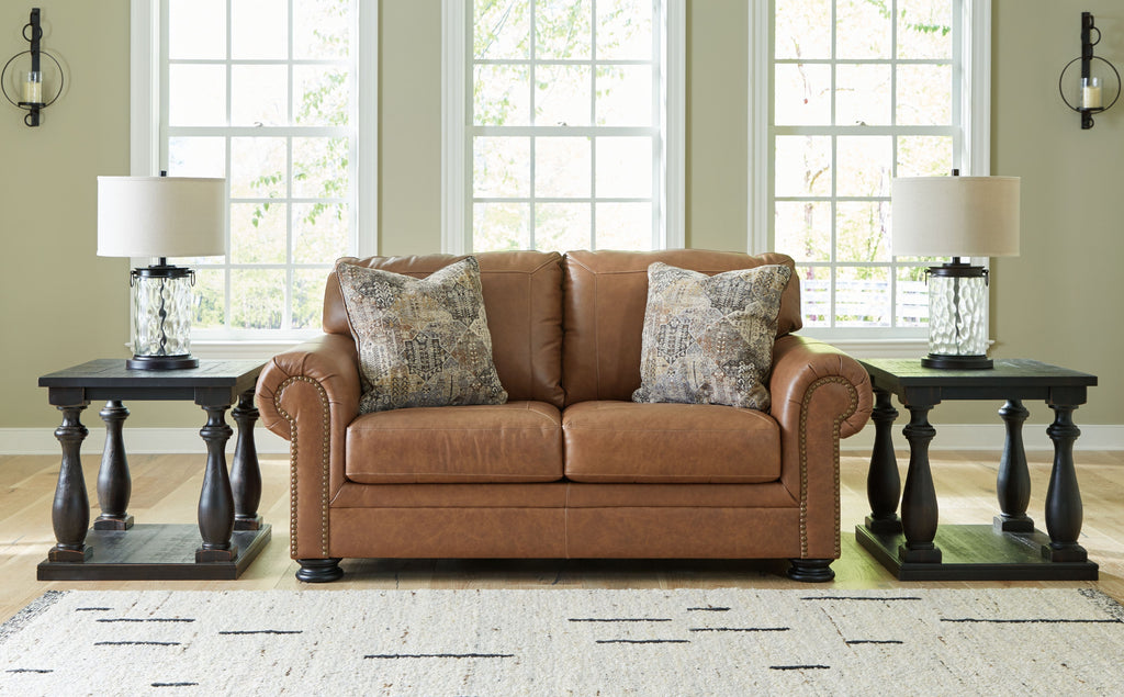 Caramel loveseat with two patterned pillows and rolled arms with nailhead trim