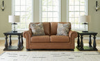 Caramel loveseat with two patterned pillows and rolled arms with nailhead trim