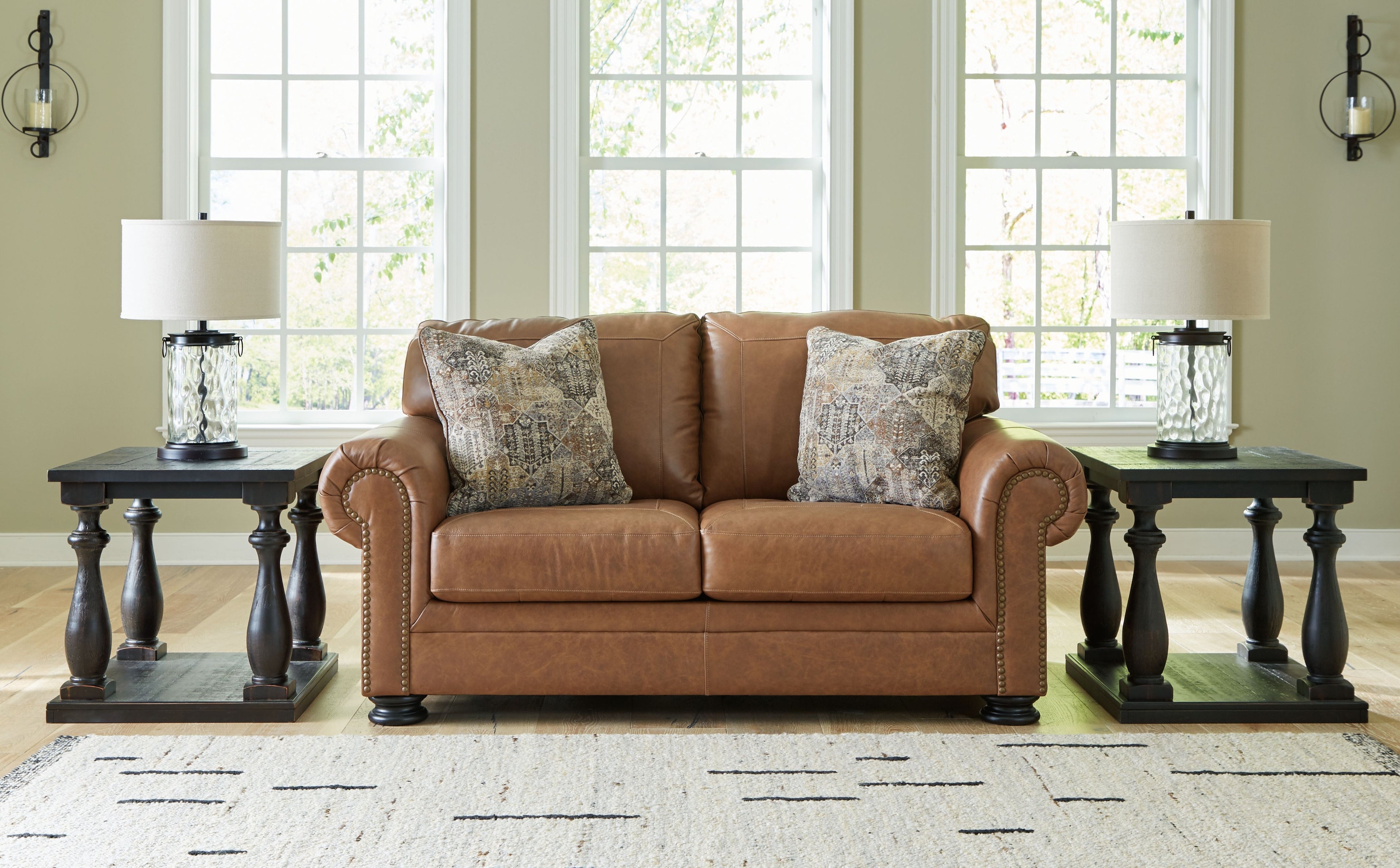 Caramel loveseat with two patterned pillows and rolled arms with nailhead trim