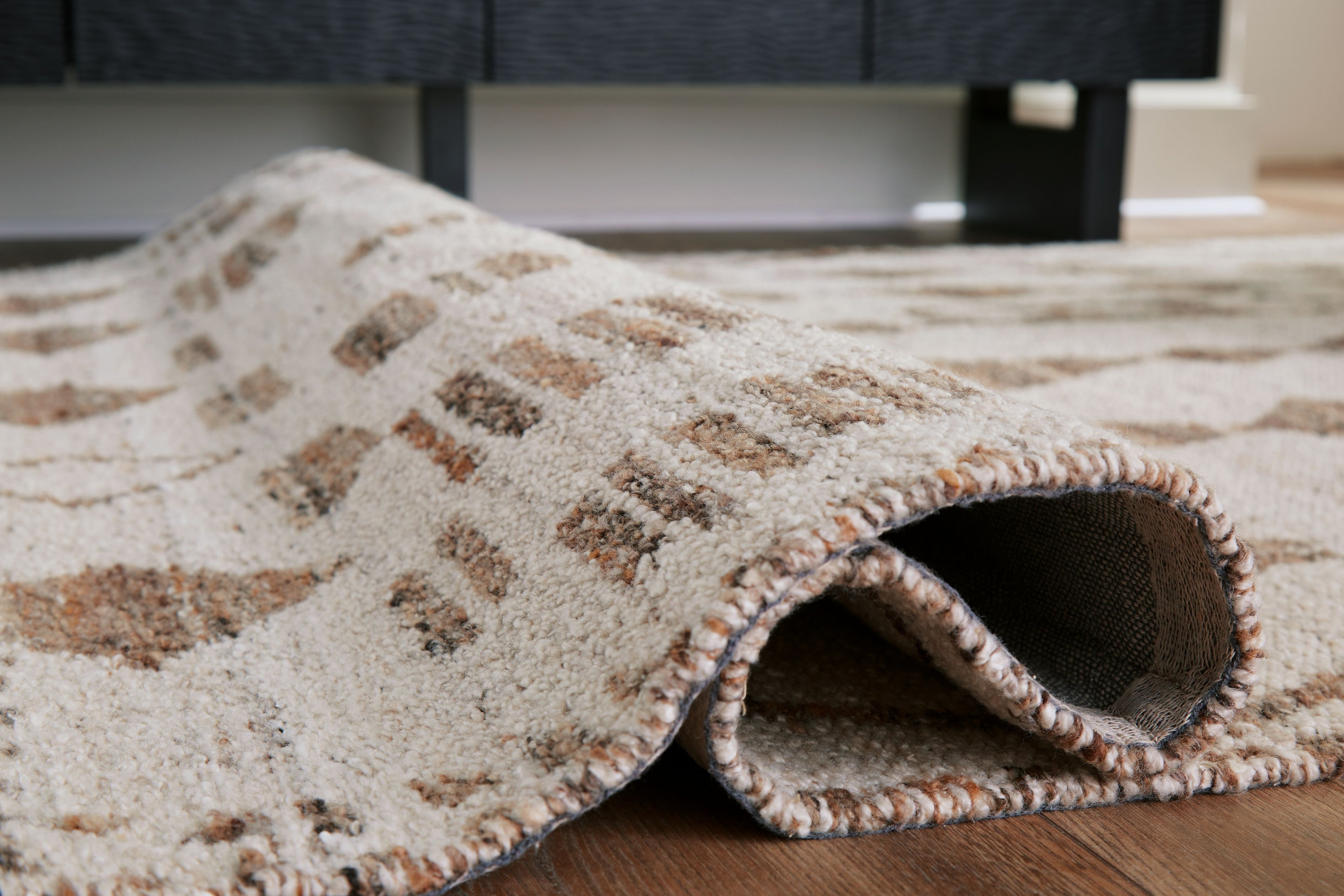Geometric area rug edge view: ivory top with dark brown diamond pattern, stitched border