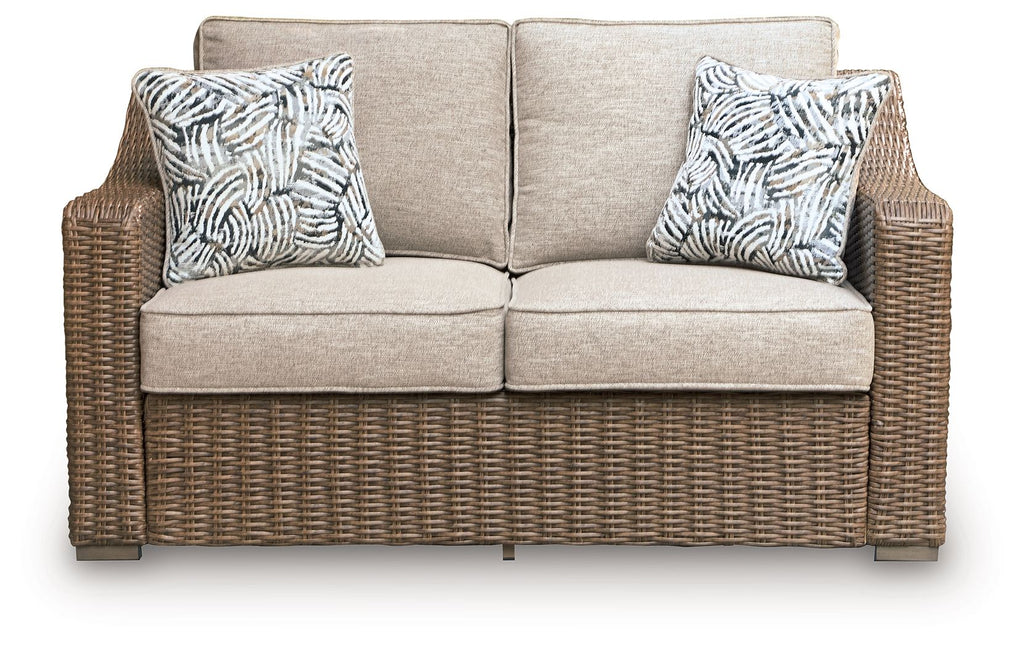 Beige loveseat with two patterned throw pillows and brown woven wicker base