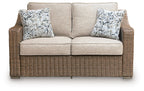Beige loveseat with two patterned throw pillows and brown woven wicker base