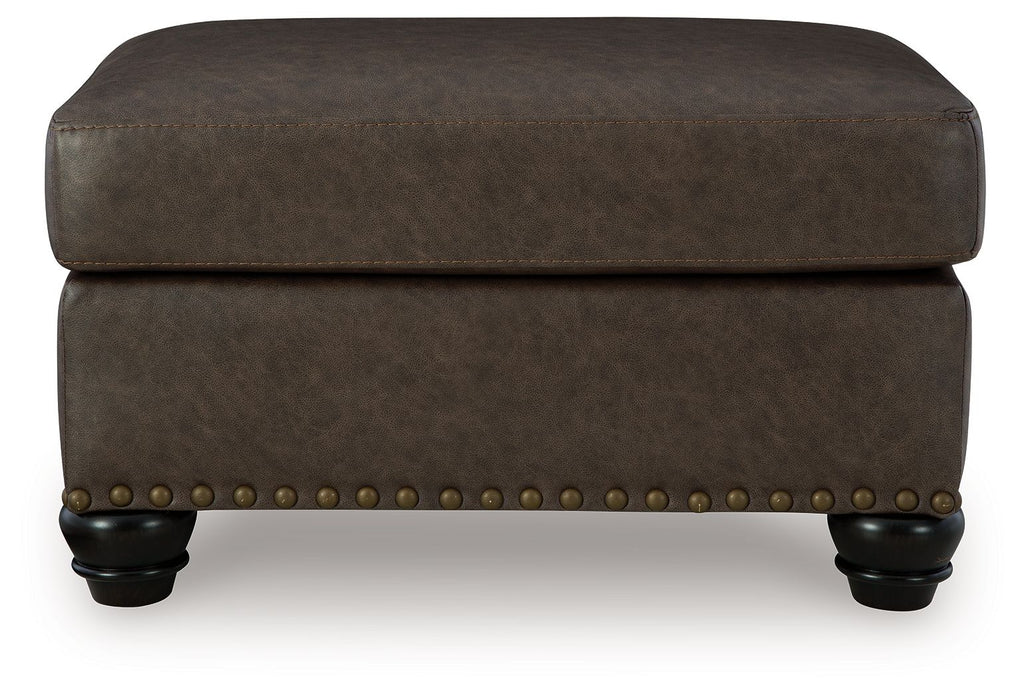 Dark brown upholstered ottoman with nailhead trim and rounded top with legs