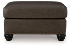 Dark brown upholstered ottoman with nailhead trim and rounded top with legs