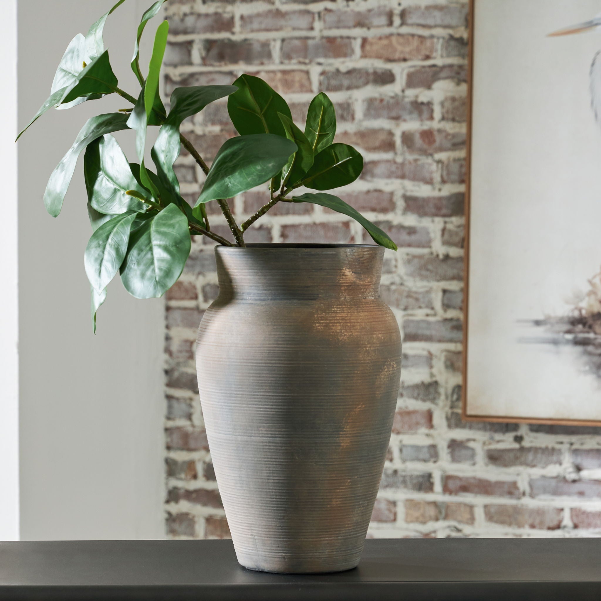 Antique gray vase with leafy greenery on a table, textured brushed finish and flared rim