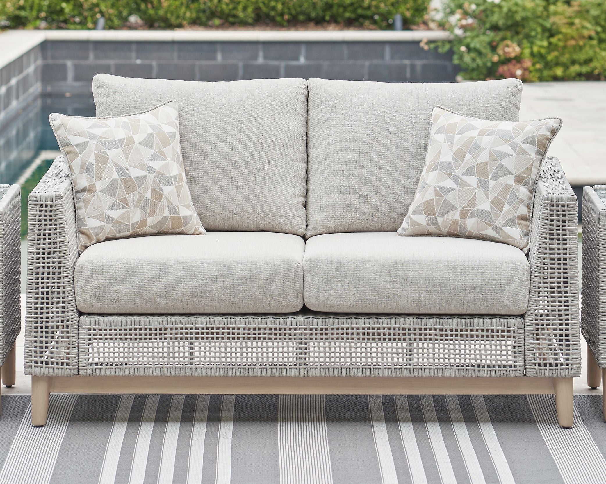 Gray woven loveseat with two seat cushions and three light patterned pillows