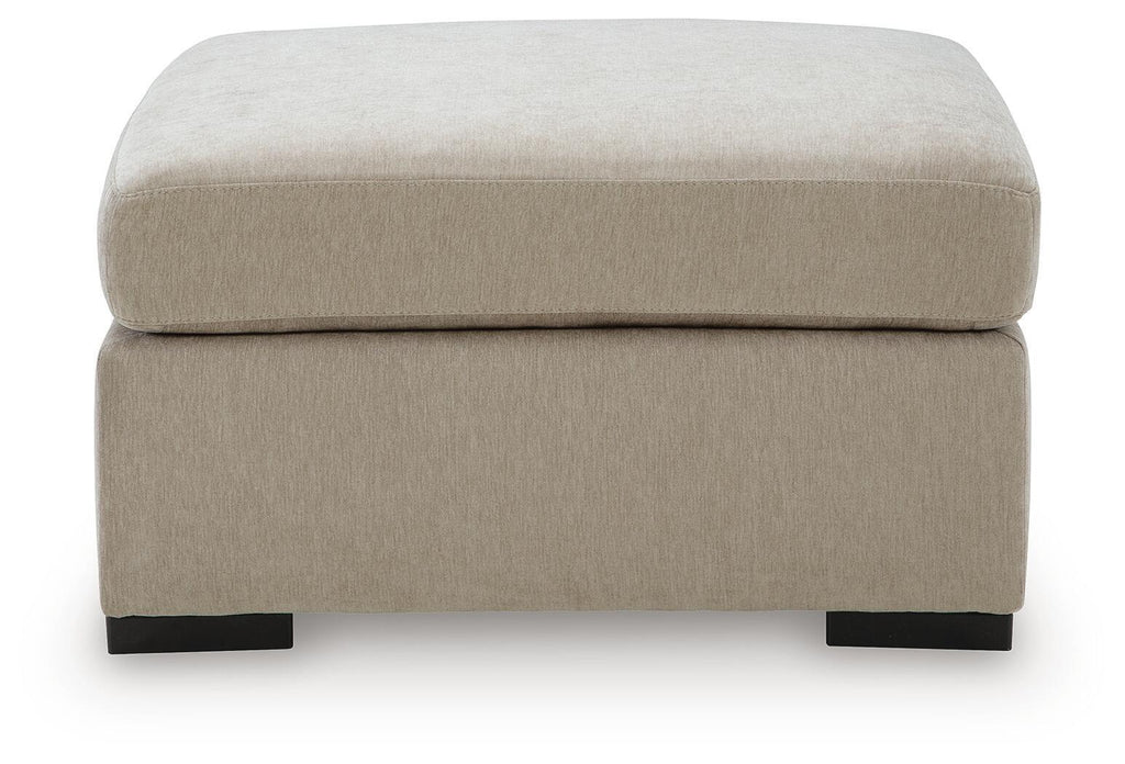 Oversized accent ottoman in light beige fabric with thick padded lid and dark block legs.